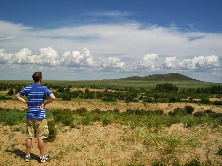Travis, hands on his hips, looking out over the green Mongolian steppe under a wide summer sky