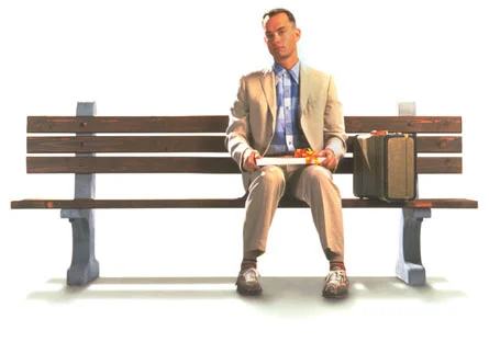 Forrest Gump (Tom Hanks) sitting on the bus-stop bench in his cream suit, suitcase beside him, box of chocolates in his lap